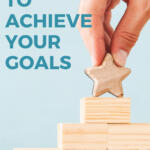 hands placing a wooden star block on top of a stack of blocks | how to achieve your goals